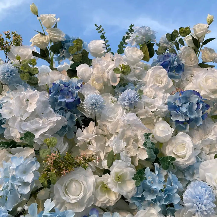 Detailed view of mixed white and blue blooms with greenery on a flower wall.