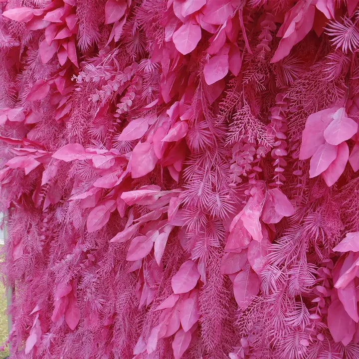 Close-up of decorative flower wall with layered pink leaves and pine fronds
