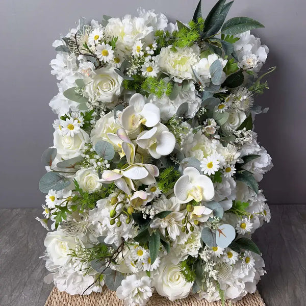Elegant white floral wall backdrop featuring roses, orchids, and greenery for weddings and parties.