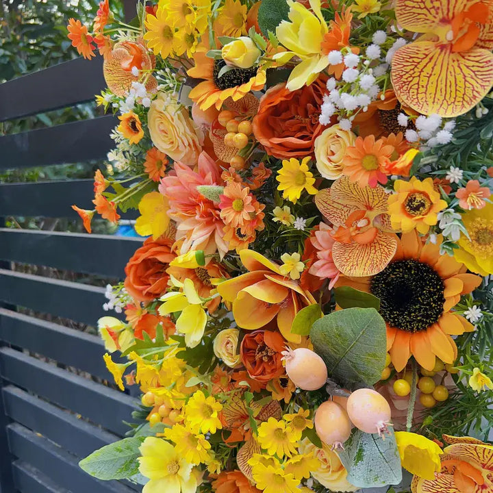 Close-up of a floral wall backdrop featuring sunflowers, yellow roses, and vibrant orange blooms for event decoration.