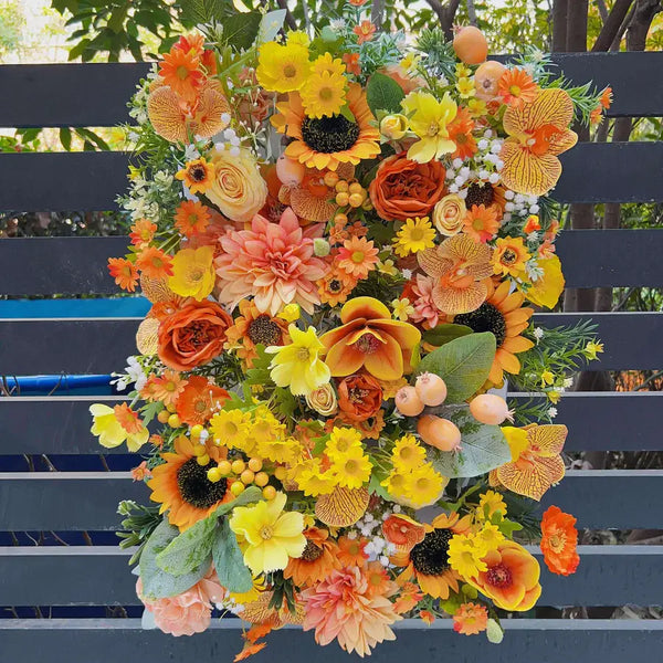 Vibrant orange floral wall backdrop with sunflowers, roses, and orchids for a lively wedding or party decoration.