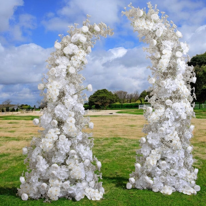 Elegant white floral arch with delicate roses and cascading flowers, set in a serene outdoor landscape, perfect for wedding ceremonies and special events.