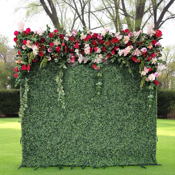 Green boxwood flower wall backdrop with cascading pink and red roses on top.